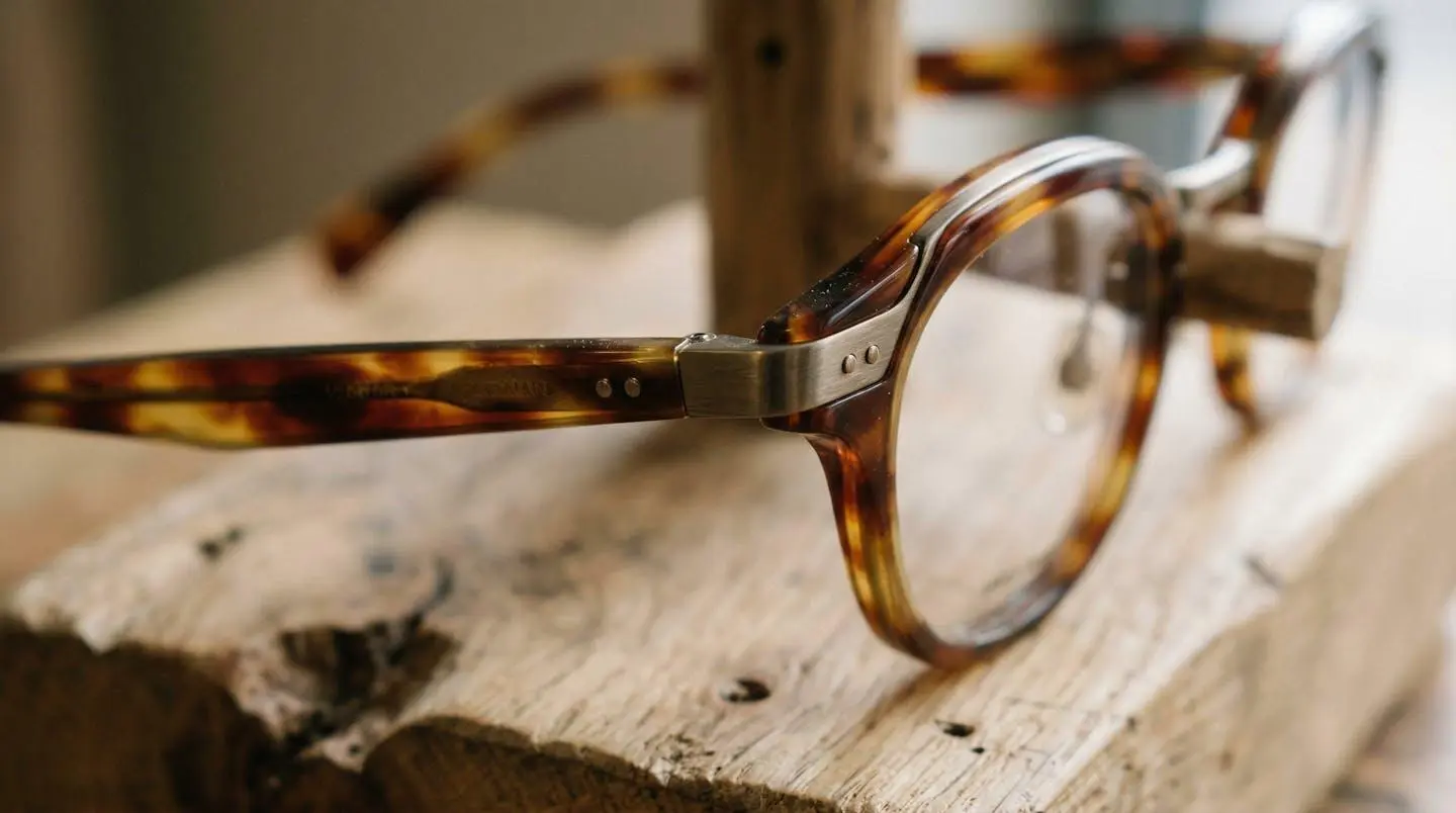 Gros plan sur plusieurs montures de lunettes aux couleurs chaudes posées sur un présentoir en bois, avec des textures d'acétate et de métal visibles